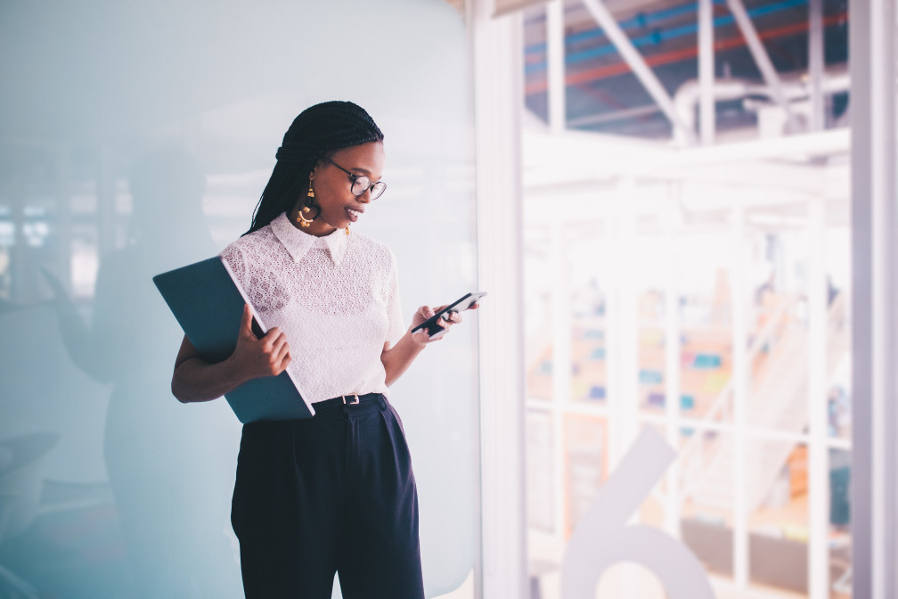 A business woman standing by the window with her smartphone